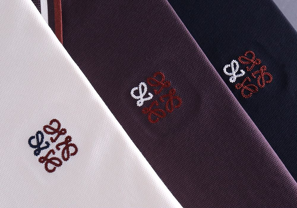 Close-up of embroidered logo detail on white, plum and navy polo shirt fabric

