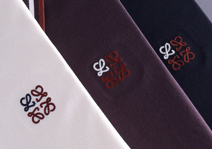 Close-up of embroidered logo detail on white, plum and navy polo shirt fabric
